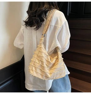 Detail view of beige canvas tote bag featuring unique fringe design and wide shoulder strap