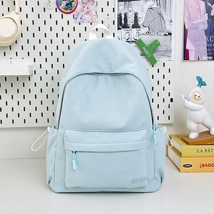 Dettaglio dello zaino in nylon azzurro con ricamo GDMN su uno sfondo decorativo da interni