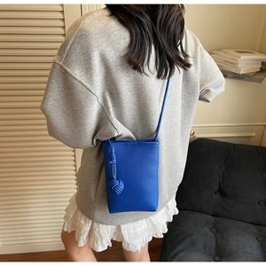 Detailed view of blue litchi grain phone bag with woven tassel on a casual model outfit