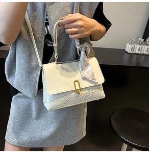 Close-up of cream woven handbag featuring golden U-buckle and decorative silk scarf handle