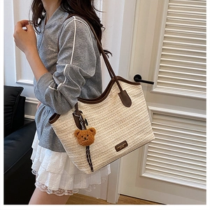 Detail showing woven straw tote bag with brown leather handles and a plush bear charm
