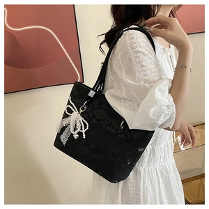 Detail of black lace tote bag with white bow accent and pearl charm on a shoulder strap
