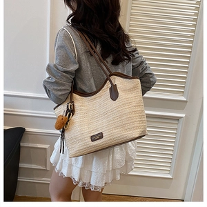 Close-up of woven tote bag showing horizontal texture, brown leather trim and bear charm