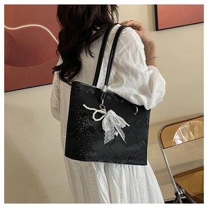 Detail of black faux leather tote with reptile embossing and pearl lace bow charm