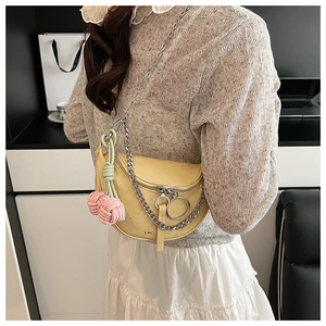 Detail of yellow saddle bag with quilted stitching, silver chain, and woven charms