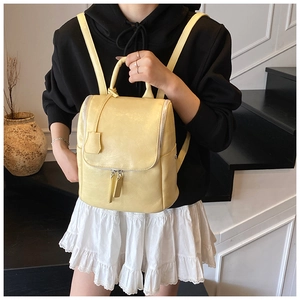 Detail view of light yellow faux leather backpack featuring a top handle and metallic zippers