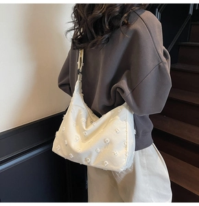 Close-up of white canvas tote with 3D pom-pom texture and adjustable shoulder strap