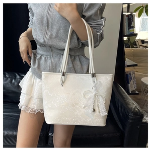 Detail of white snakeskin pattern tote bag with lace bow and pearl heart charm