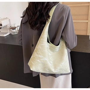 Detailed back view of a glossy beige pleated hobo bag worn in a modern cafe setting