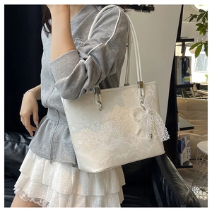 Close-up of white tote bag with snake skin embossing and pearl bow charm accessory