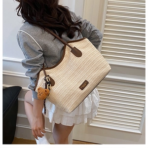 Detail of woven straw tote bag with brown leather handles and a cute bear charm