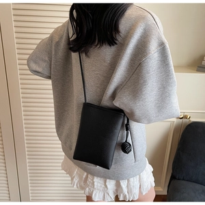 Close-up of a black lychee texture crossbody phone bag with an elegant knot pendant charm