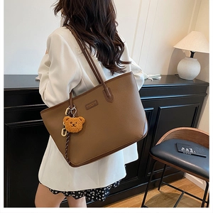Dettaglio della borsa tote in pelle marrone scuro con ciondolo a orsetto e texture