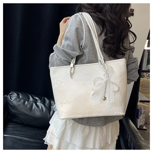Close-up of a white tote bag with faux snake skin texture and pearl bow charm