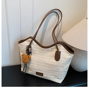 Detail of woven straw tote bag with brown leather handles and a plush bear pendant