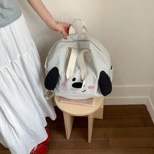 Detail of cute embroidered dog face on grey nylon backpack atop a wooden stool