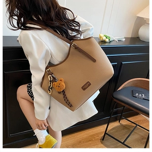 Detail of khaki pebbled leather tote bag with brown plush bear charm and chain strap