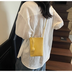 Detail of yellow pebble leather mini crossbody phone bag with knot woven charm on a model
