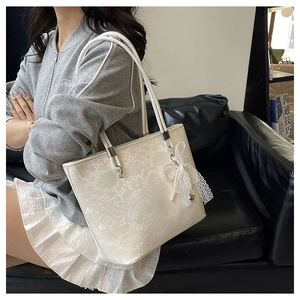 Detail of white tote bag with snake skin texture, pearl charm and lace bow