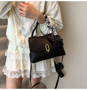 Detail of black woven leather handbag with gold oval clasp and silk scarf handle
