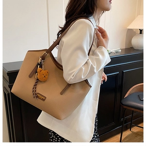 Detail view of large khaki tote bag with litchi texture and cute bear charm on shoulder