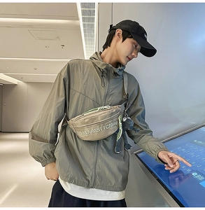 Close-up of beige nylon chest bag with embroidery and a plush frog charm on model