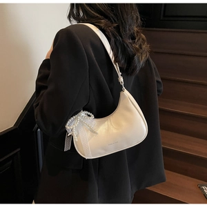 Detail der cremefarbenen Tasche mit Spitzen-Schleife und Perlen auf schwarzem Blazer