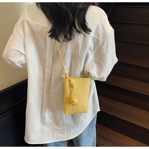 Detail of yellow pebble leather phone bag with unique woven knot strap on white shirt