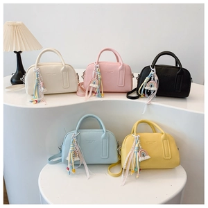 Five small Boston style handbags in various colors displayed on a white tiered stand