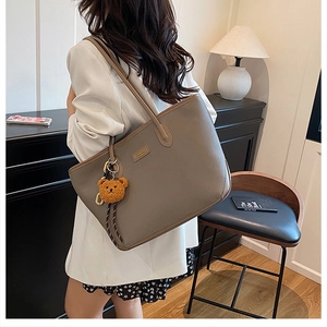 Dettaglio della borsa tote in pelle marrone con ciondolo a orsetto e placca in metallo