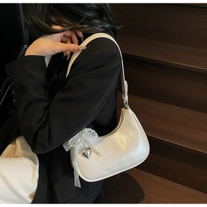 Nahaufnahme der hobo-tasche mit perlmuttglanz, perlen-schleife und herzanhänger auf holz
