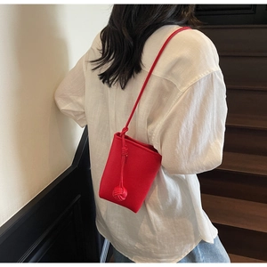 Close-up of a red litchi texture leather crossbody bucket bag with leather knot detail