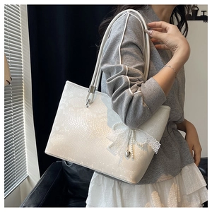 Detail of white snakeskin tote bag with lace bow, pearl chain and heart pendant