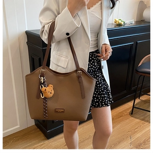 Detail of brown litchi pattern leather tote bag featuring a cute teddy bear pendant