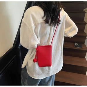 Red pebbled leather phone bag with knot detail shown against a modern staircase