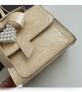 Detail of cream leather handbag with decorative bow and pearl heart charm accessory