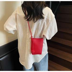 Detail of red lychee textured leather mobile bag with decorative knotted strap ball