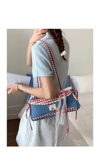 Detail of denim shoulder bag with red gingham trim and cherry patch on model