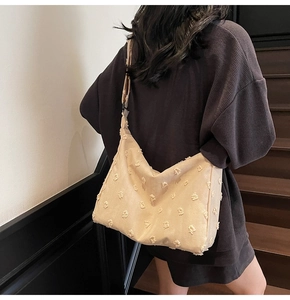 Detail of beige canvas tote featuring 3D tufted floral textures and wide shoulder strap