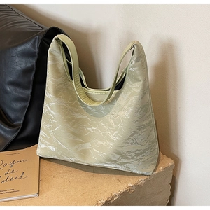 Detailed view of light green pleated satin tote bag with wide shoulder strap on stone