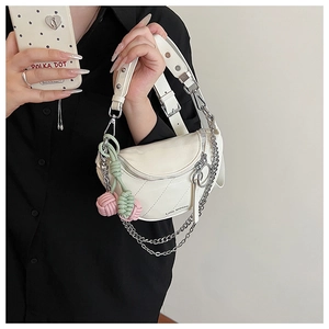 Detail of cream saddle bag with diagonal quilting, silver chain, and woven knot charm