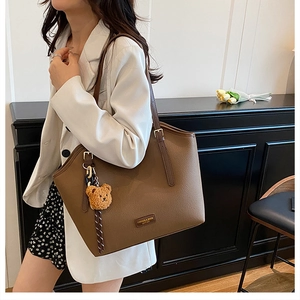 Detail of coffee brown leather tote bag with metallic logo and cute bear charm pendant