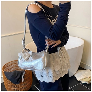 Detail of silver metallic pleated hobo bag featuring lace bow and pearl heart charm
