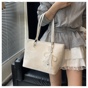 White tote bag with lace texture detail, twin straps and pearl bow charm shown in a home setting