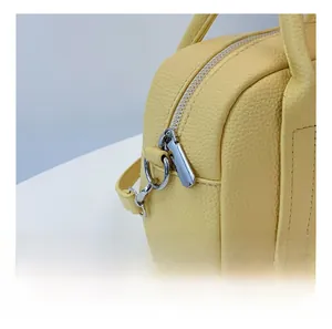 Detail showing smooth silver metal zipper and lychee grain texture on yellow handbag
