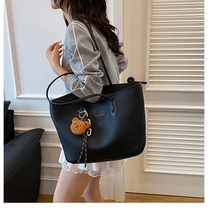 Dettaglio di una borsa tote nera in pelle con un simpatico ciondolo a forma di orso bruno