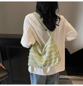 Detail view of light green canvas tote bag with stylish frayed edge design worn by model