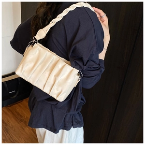 Detail view of cream-white ruched leather shoulder bag with wide woven strap on model