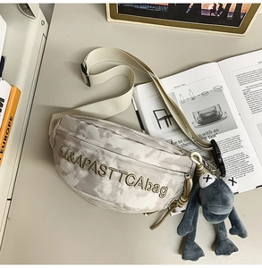 Detailed close-up of grey tie-dye chest bag with embroidery and plush frog keychain accessory