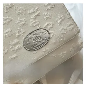 Detail der cremeweißen Nylontasche mit floraler Textur und ovaler silberner Metallplakette